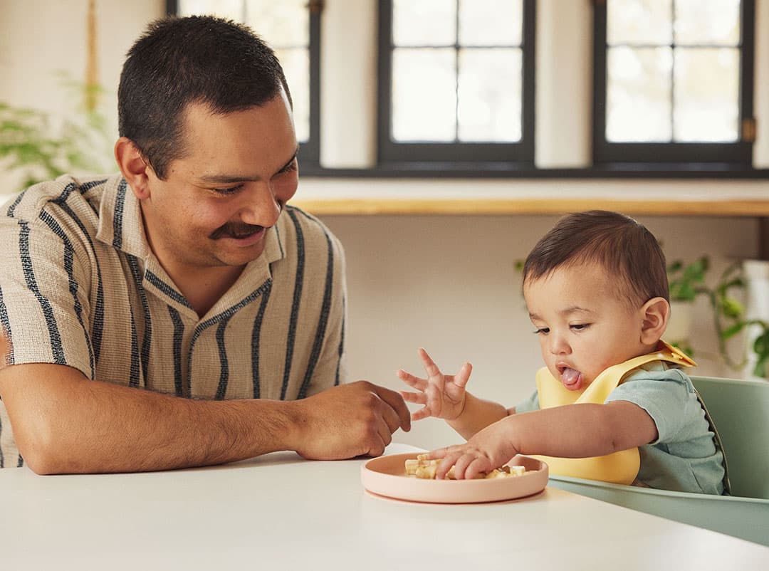 Baby sitting with their father touching food